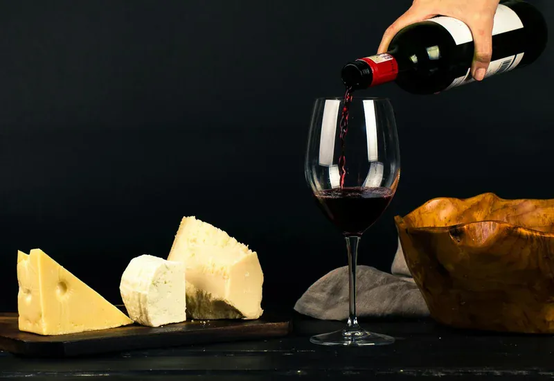 Vino versato in un calice accanto a un tagliere di formaggi