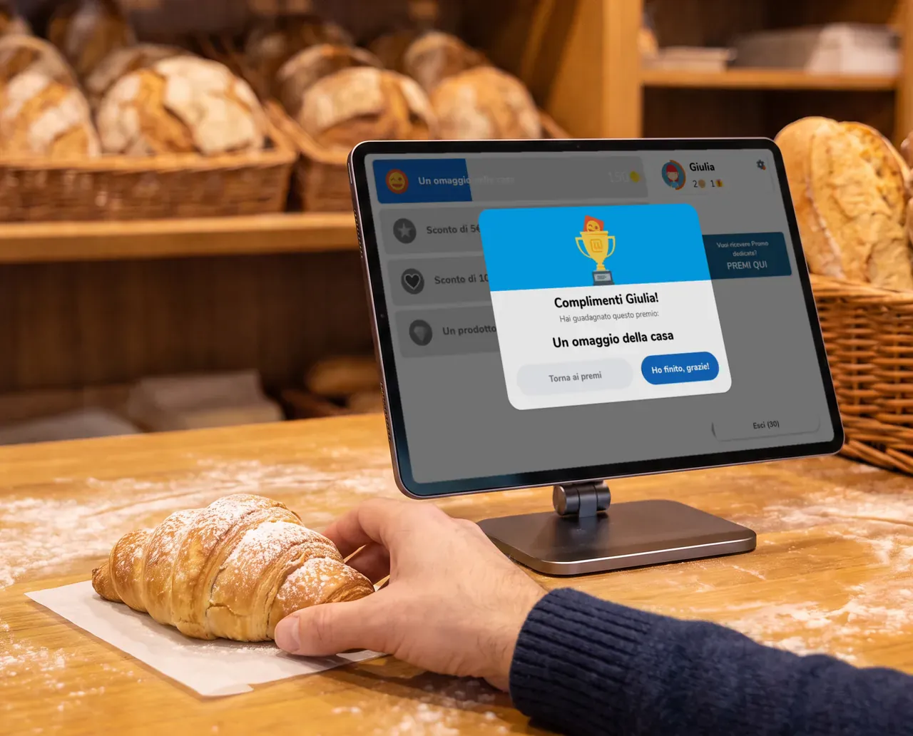 Fotografia illustrativa generata: una mano prende la brioche mentre il Chiosco conferma il Premio ritirato, «Un omaggio della casa», con la schermata vera