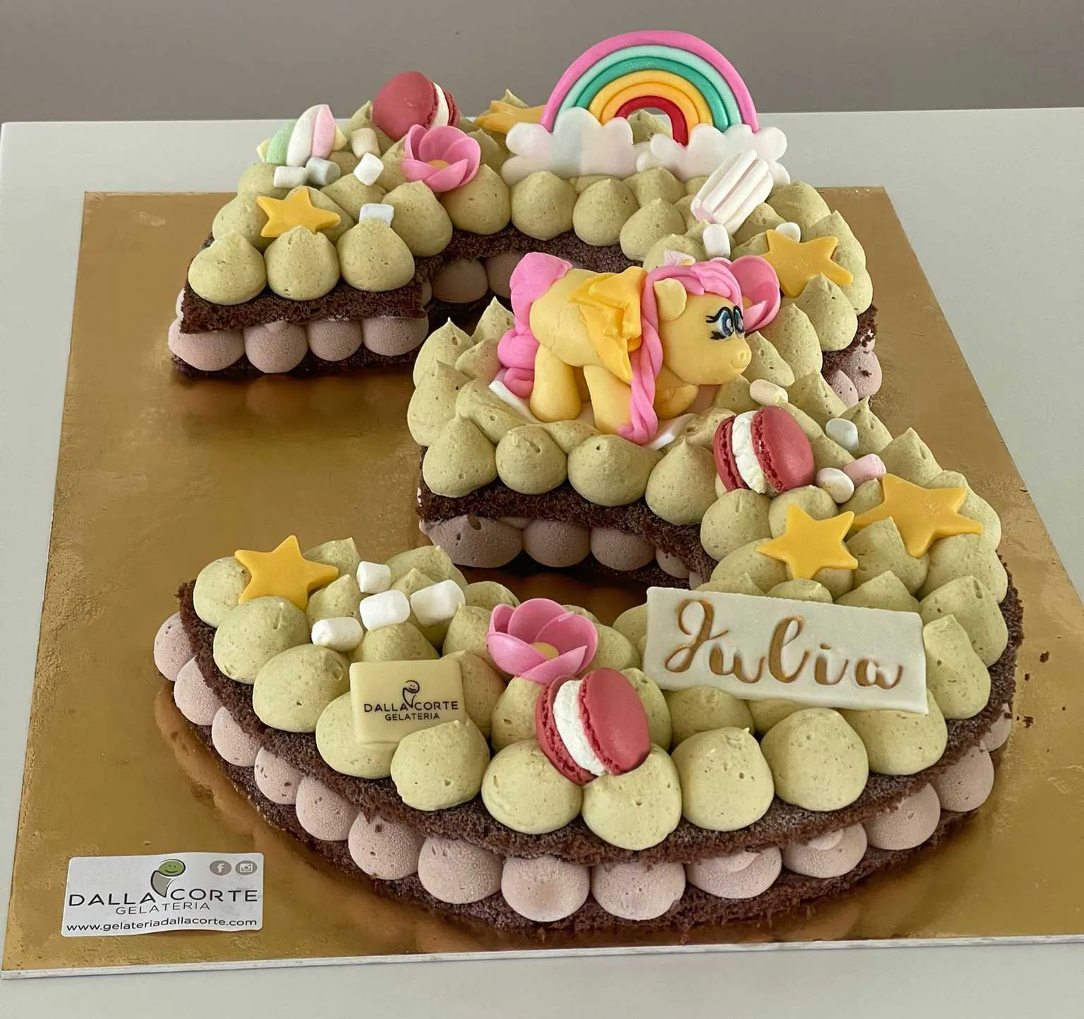 Una torta di compleanno a forma di numero, decorata con meringhe e un arcobaleno